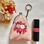 Pink floral embroidered coin purse next to lipstick