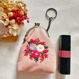 Pink floral embroidered coin purse next to lipstick