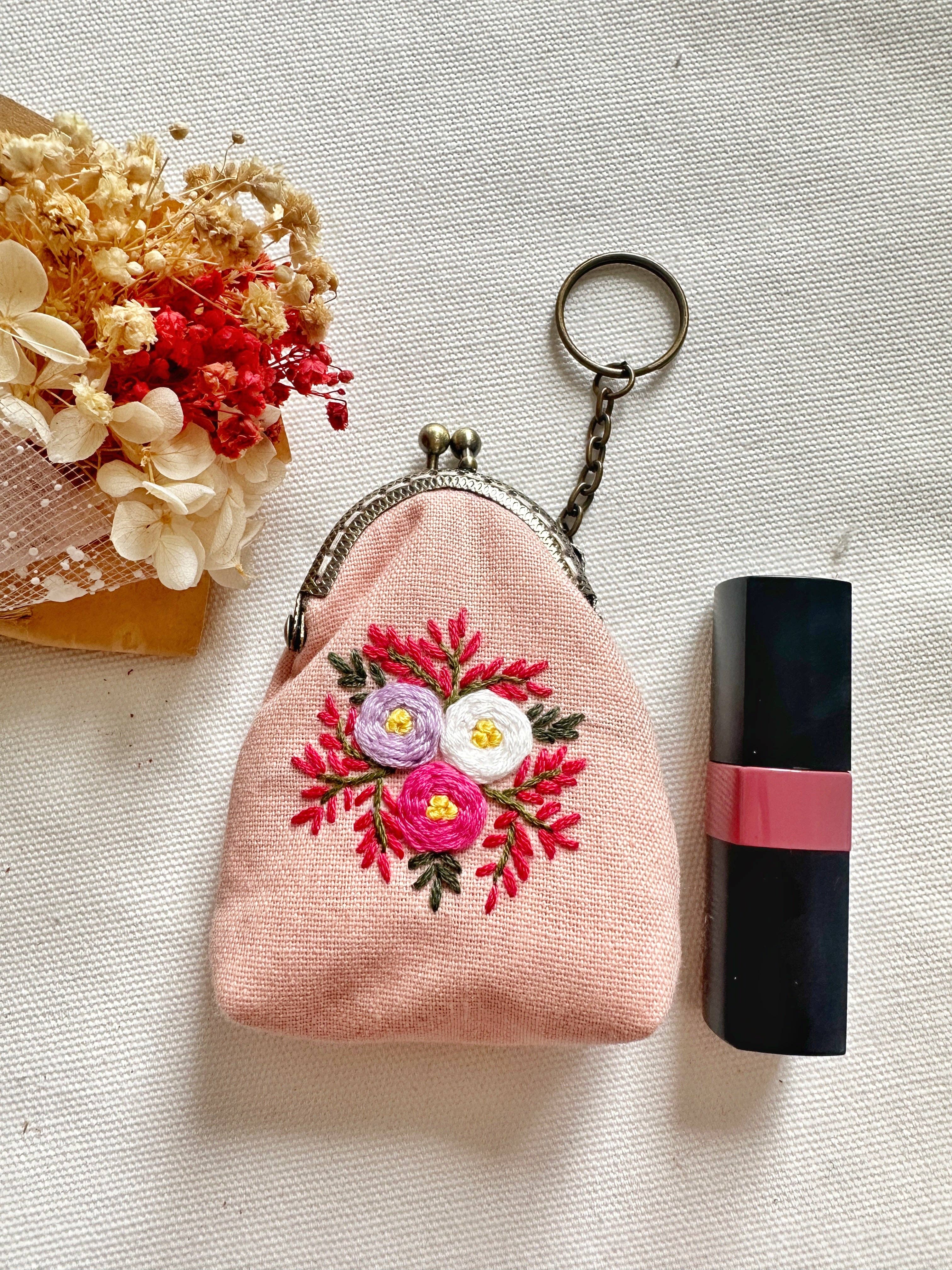 Pink floral embroidered coin purse next to lipstick