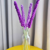 Crocheted lavender flowers in glass vase on yellow table