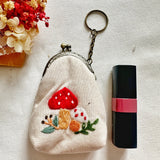 Embroidered mushroom coin purse next to lipstick