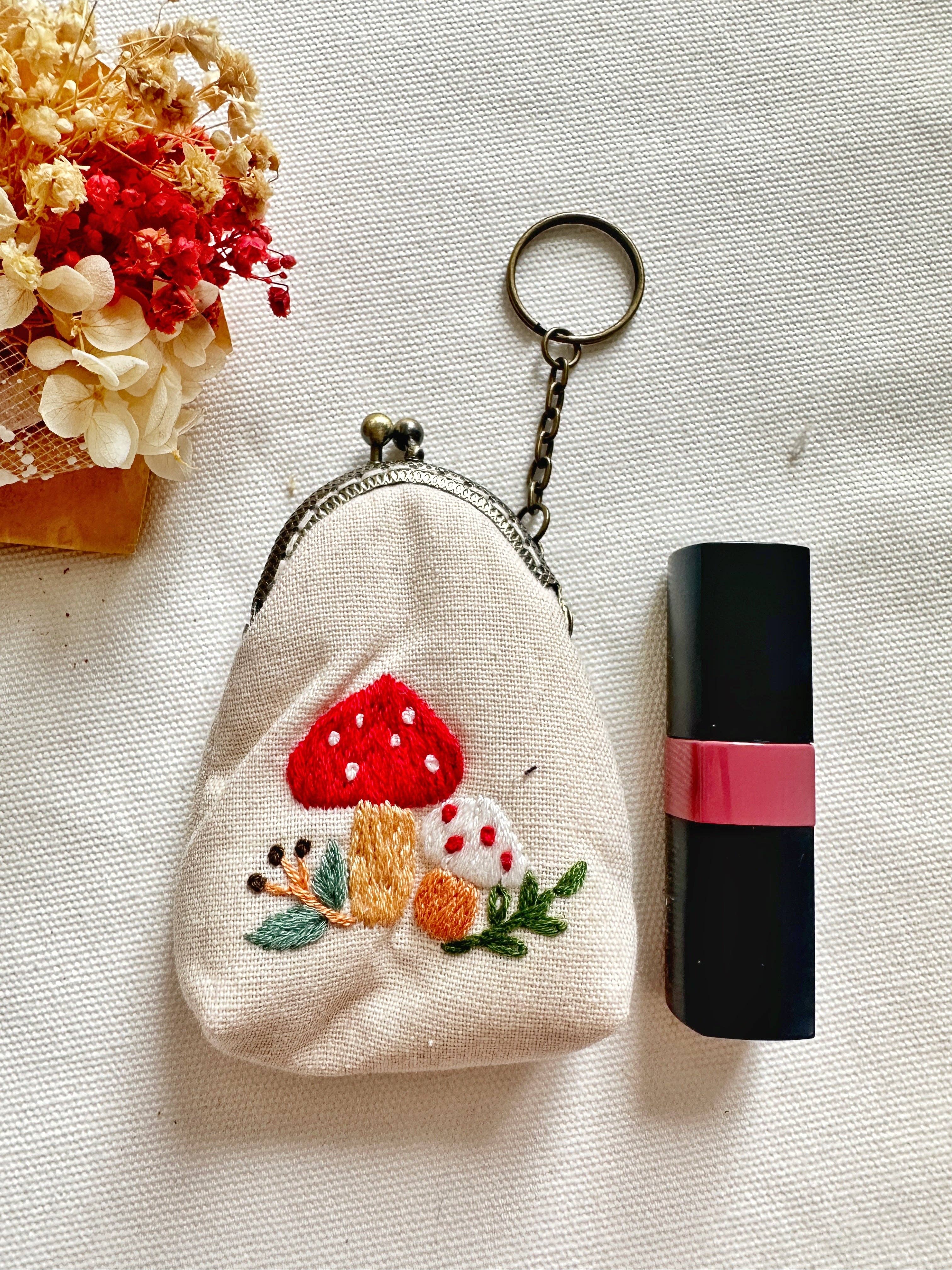 Embroidered mushroom coin purse next to lipstick