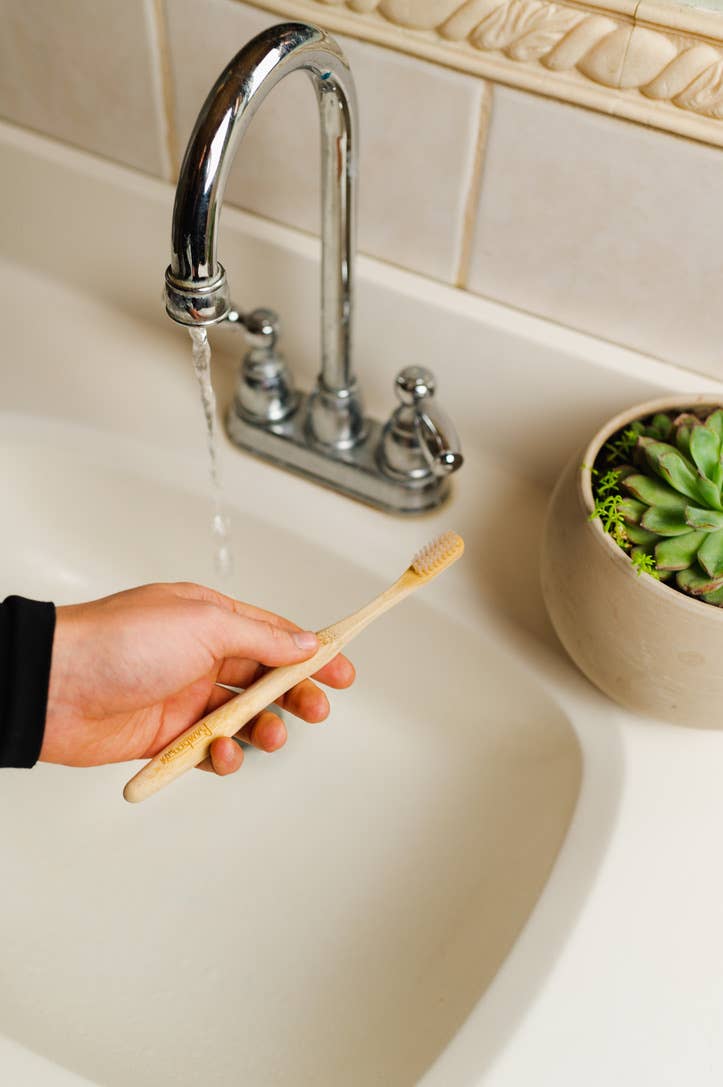 Hand holding a toothbrush under running water in a sink.