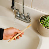 Hand holding a toothbrush under running water in a sink.