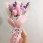 Crocheted flower bouquet in pink wrapping, held by a hand.