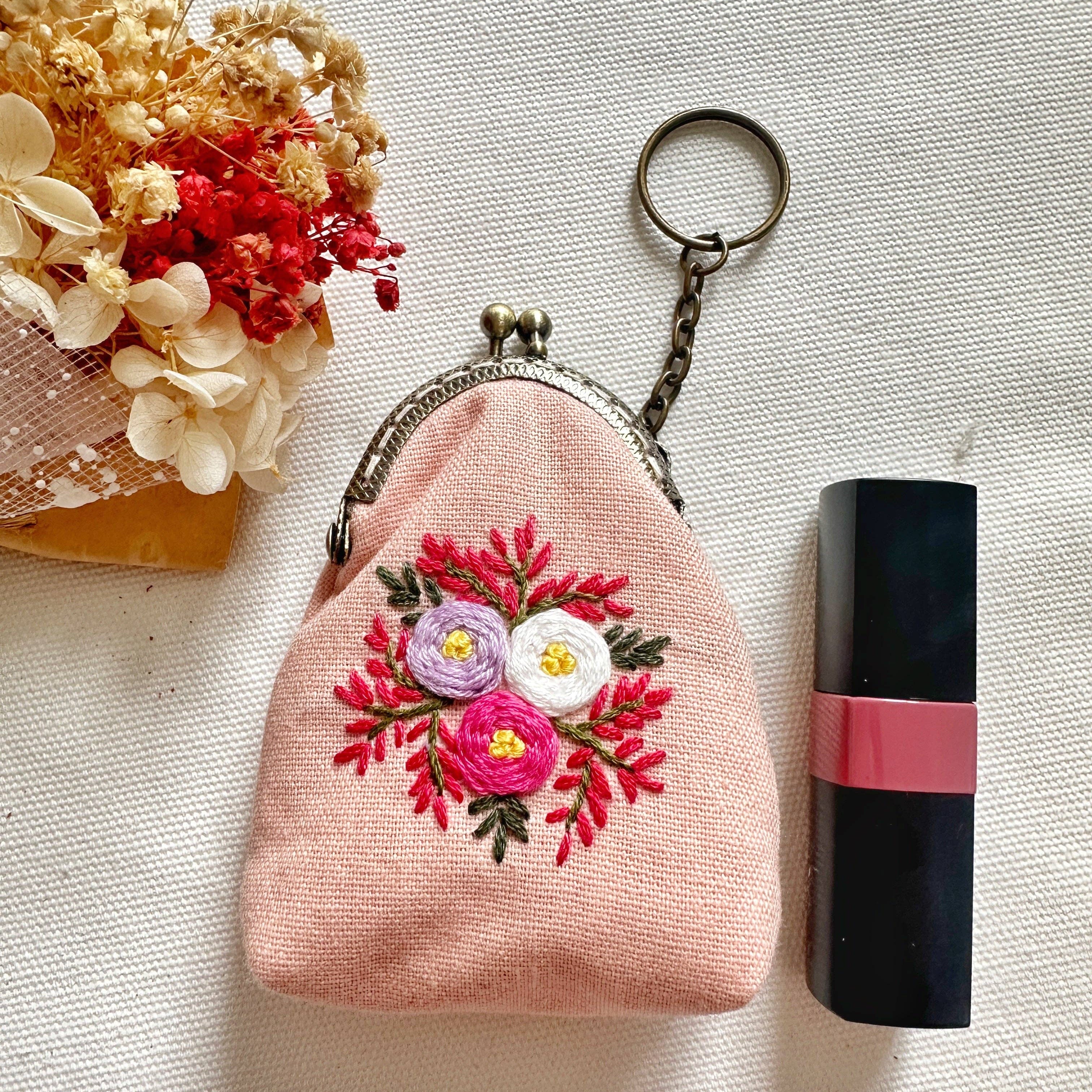 Pink floral embroidered coin purse next to lipstick