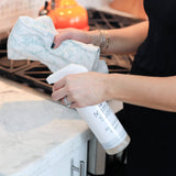 Woman cleaning kitchen counter with spray bottle and cloth.