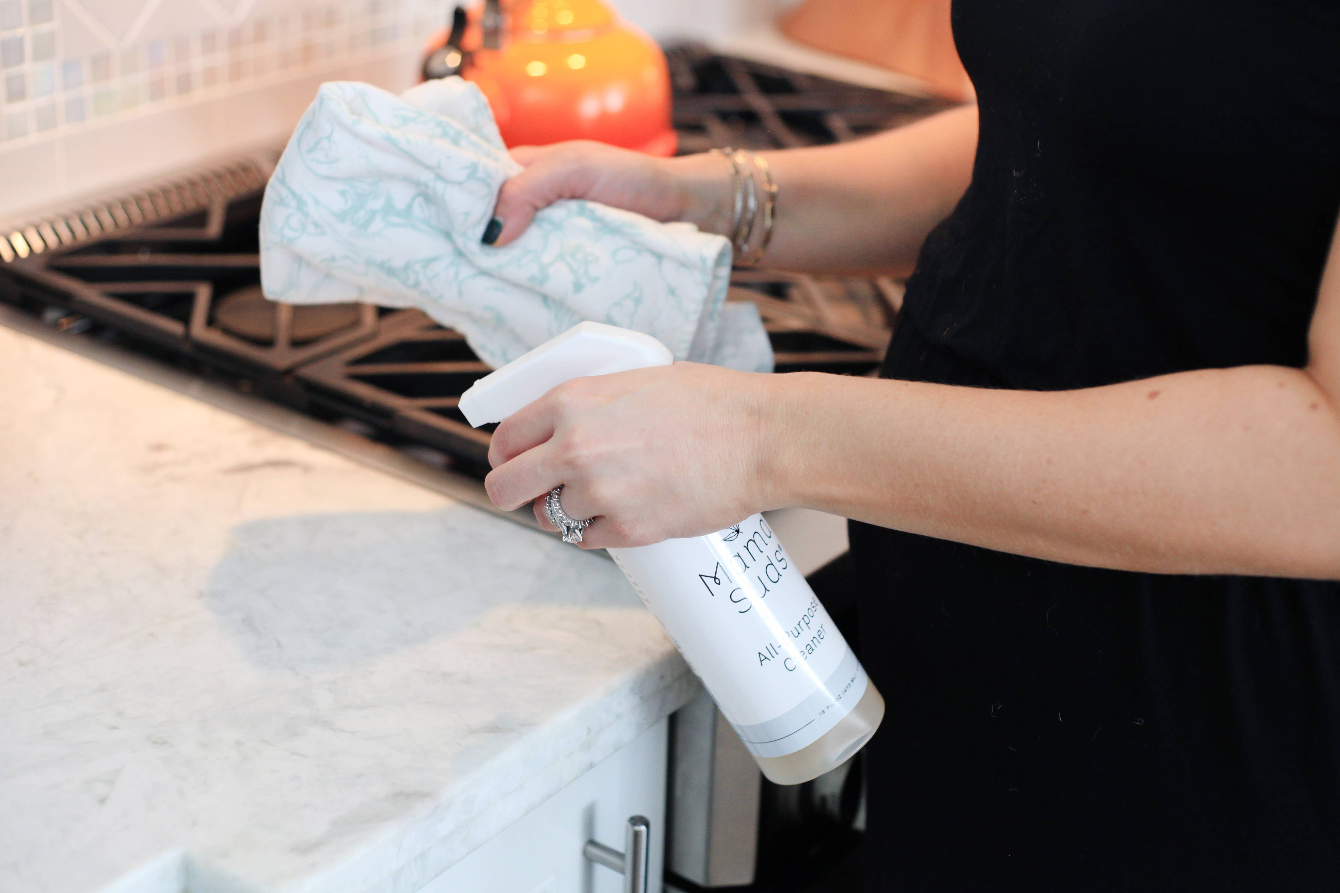 Woman cleaning kitchen counter with spray bottle and cloth.