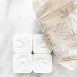 Four square soap tablets with leaf design next to a linen bag.