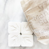 Four square soap tablets with leaf design next to a linen bag.