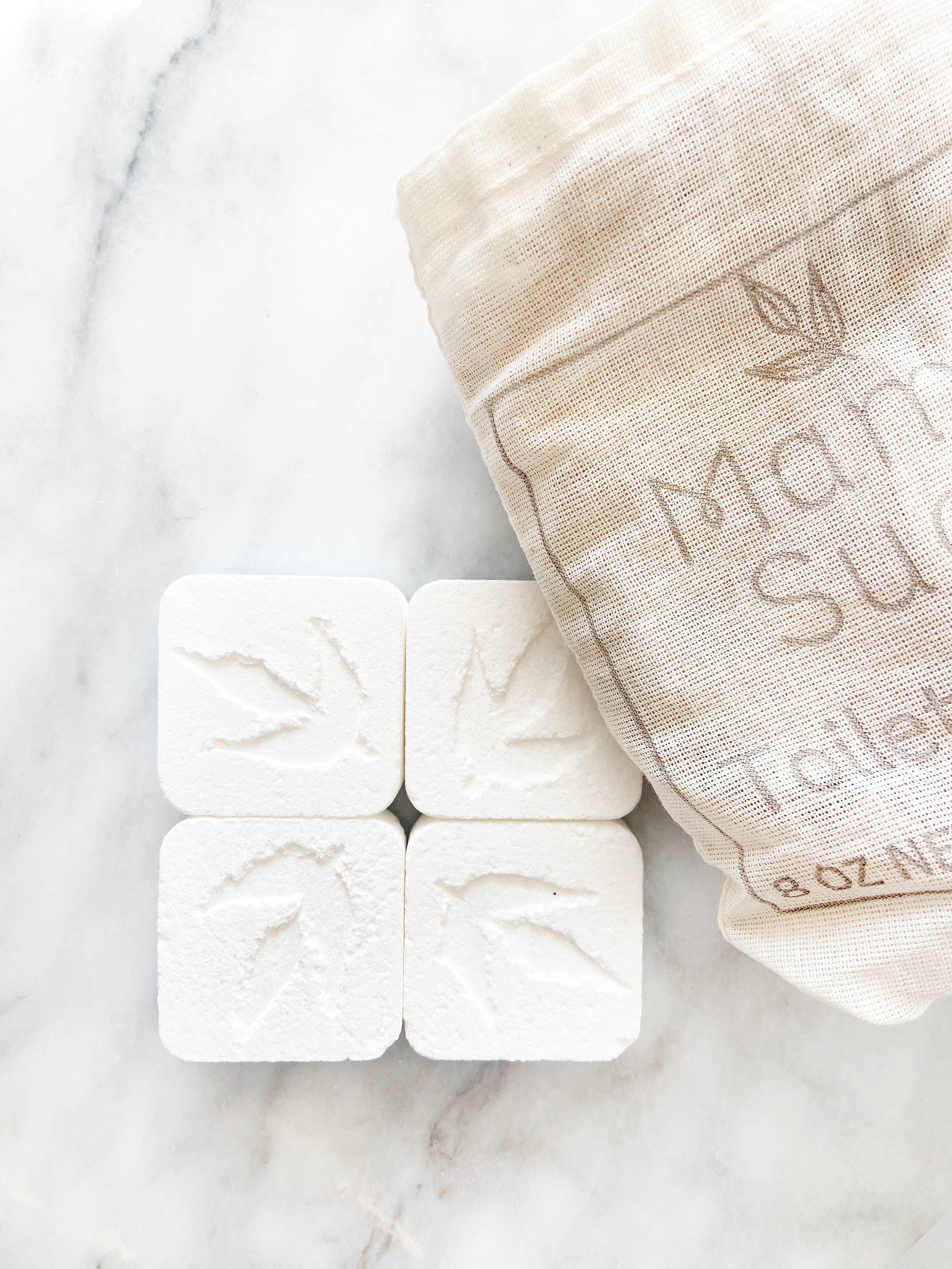 Four square soap tablets with leaf design next to a linen bag.