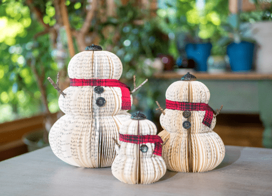 Three book-page snowmen with scarves and twig arms.