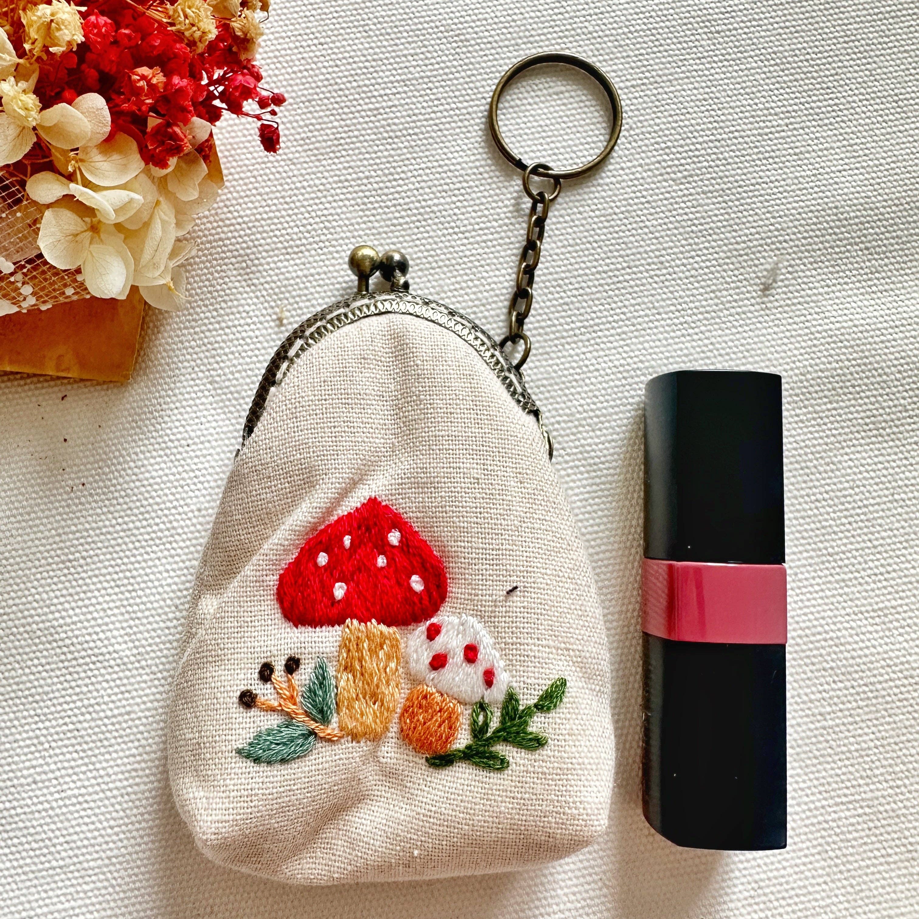 Embroidered mushroom coin purse next to lipstick