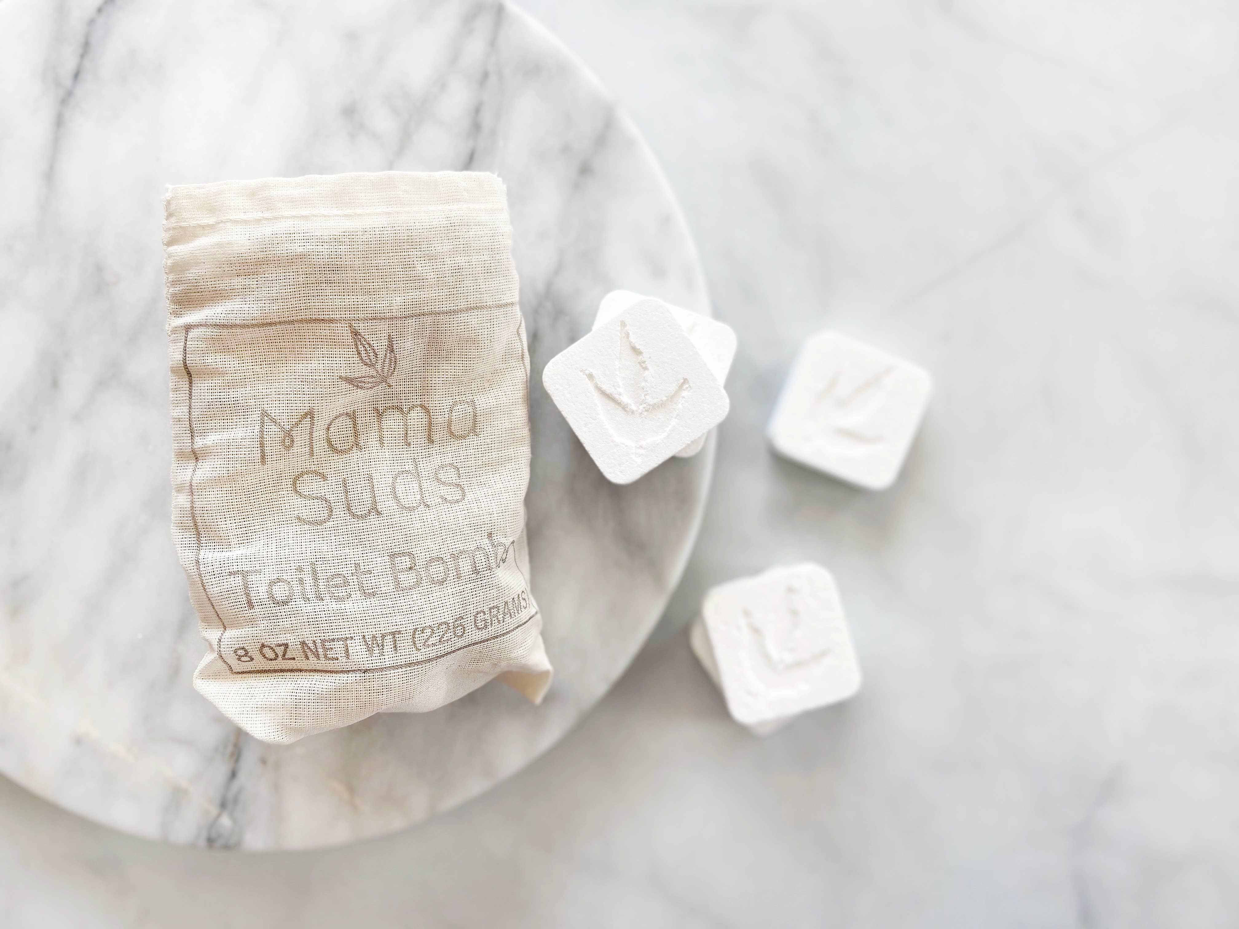 Bag of toilet bombs and three individual tablets on marble.