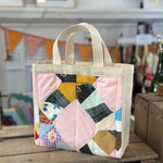 Quilted tote bag with cream handles on a wooden surface.