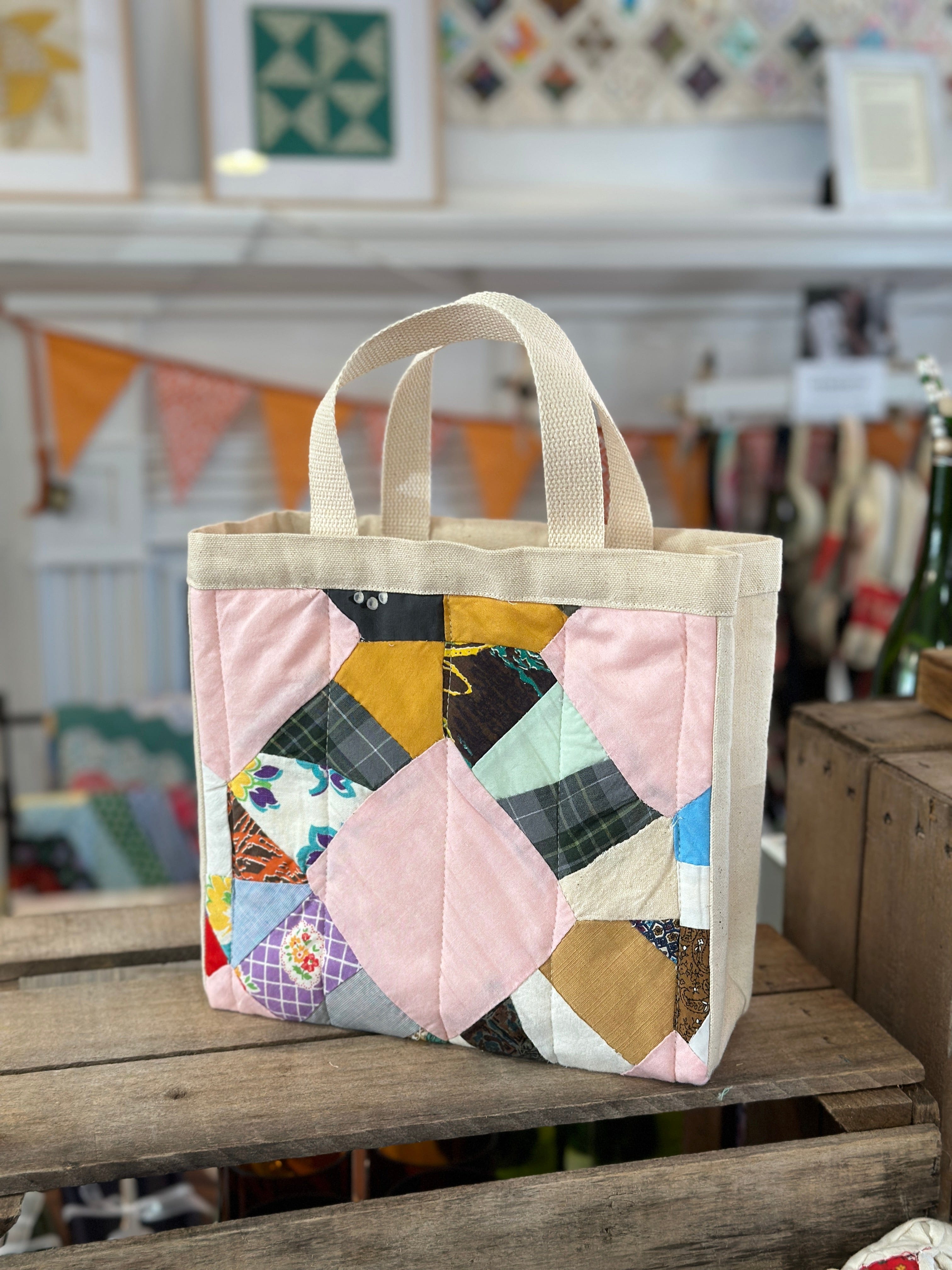 Quilted tote bag with cream handles on a wooden surface.