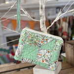 Quilted green and floral clutch hanging from a branch.