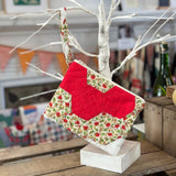 Quilted floral and red clutch hanging from a white branch.