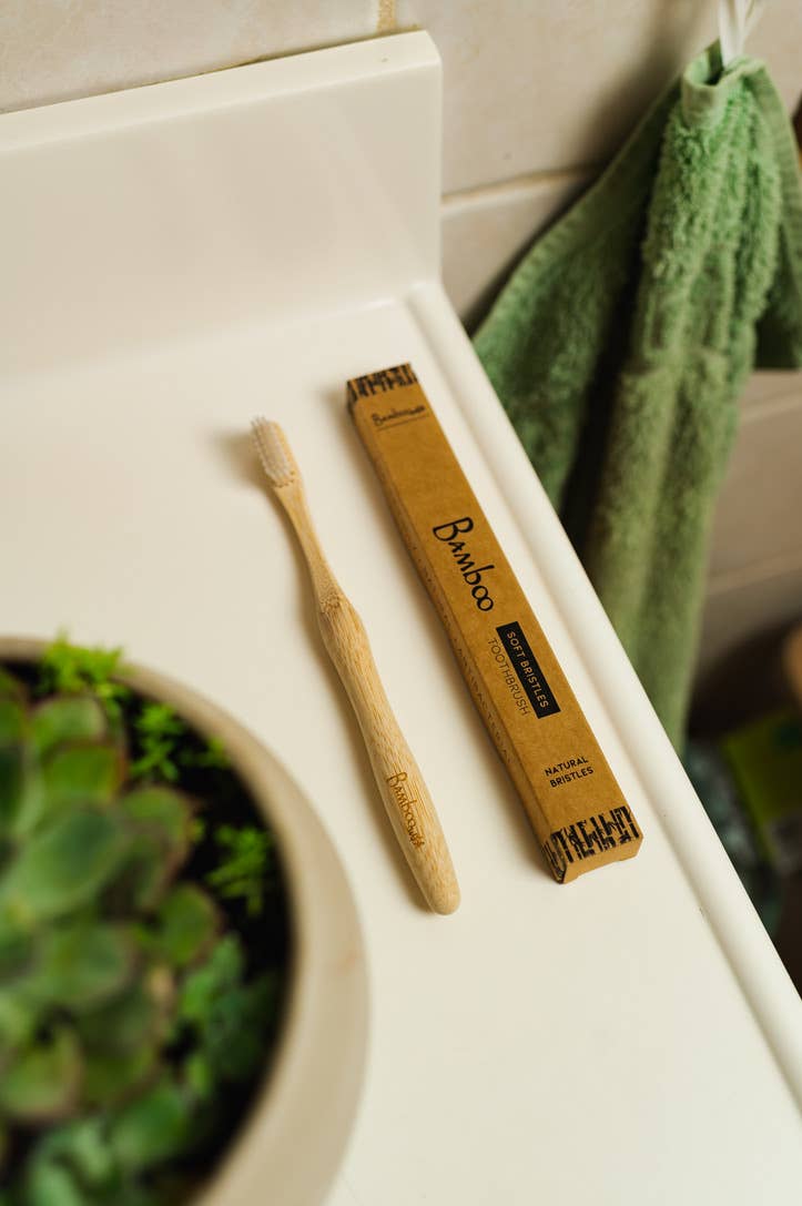 Bamboo toothbrush and packaging on a bathroom counter.