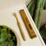 Bamboo toothbrush and packaging on a bathroom counter.