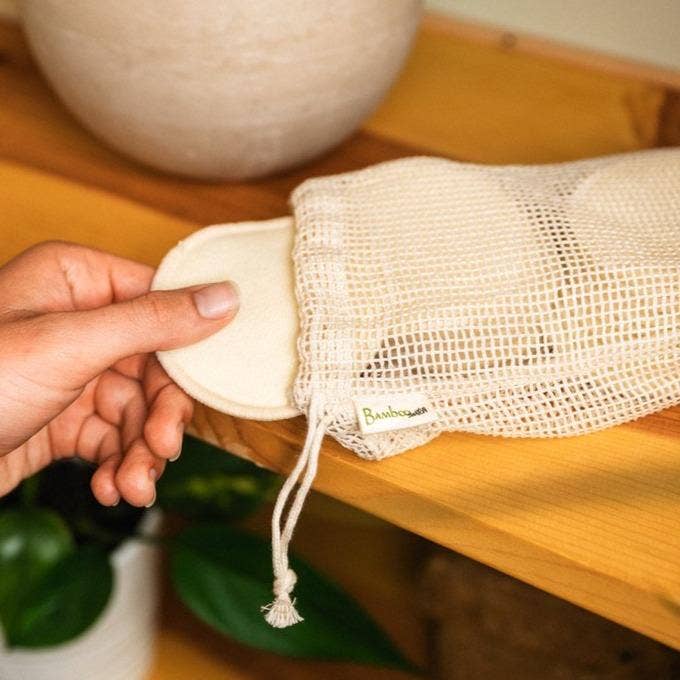Hand holding a reusable cotton pad next to a mesh bag.