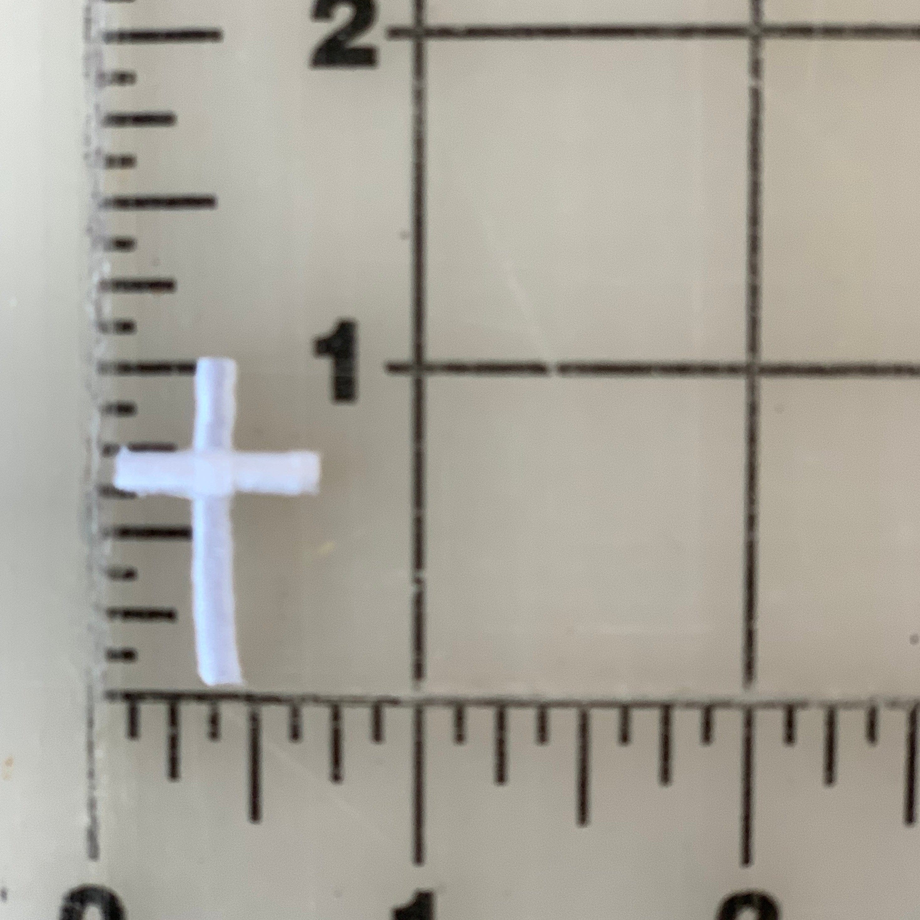 Small white cross next to a ruler.