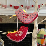 Red and pink fabric bird ornaments hanging on a white tree