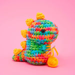 Crocheted rainbow dinosaur toy with yellow spines and a ball of yarn.